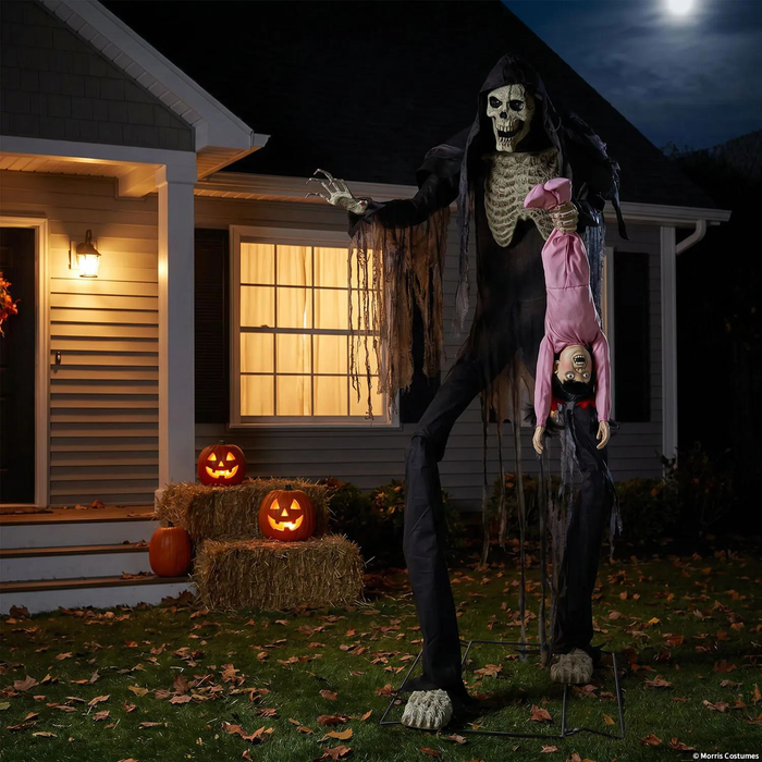 Animatronic esqueleto gigante con niña frente a una casa decorada para Halloween