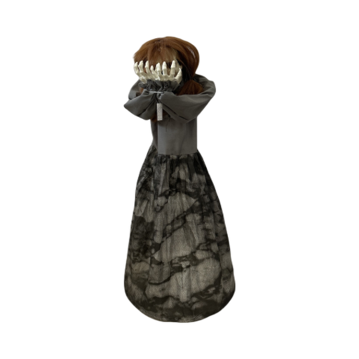 Animatronic niña con vestido gris y manos de esqueleto cubriendo la cara