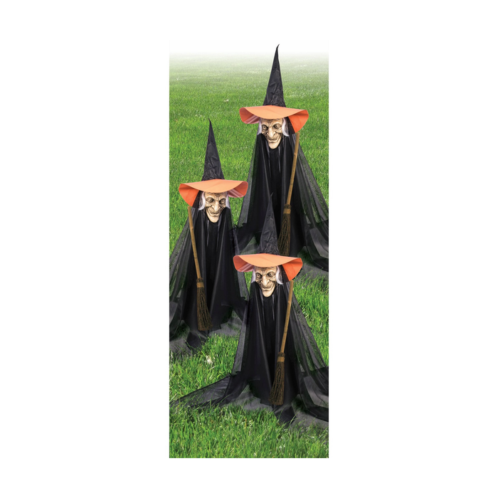 Tres brujas decorativas con sombrero naranjo y capa negra en un jardín
