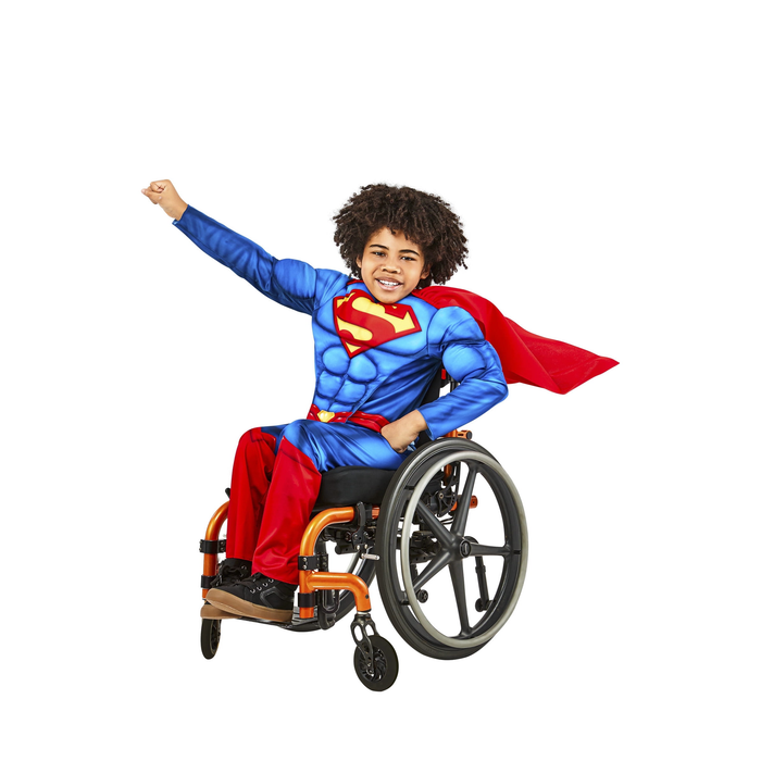 Niño en silla de ruedas con disfraz de Superman adaptado: polera azul musculosa, pantalón rojo y capa roja